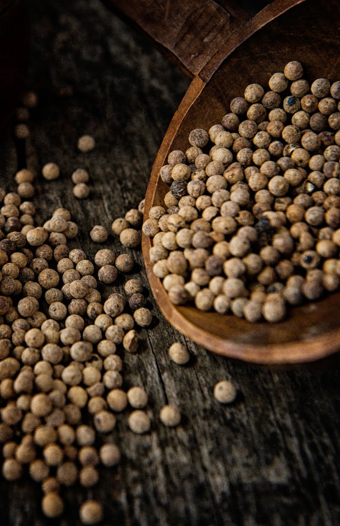 A rustic wooden spoon filled with whole peppercorns on a dark wooden surface.