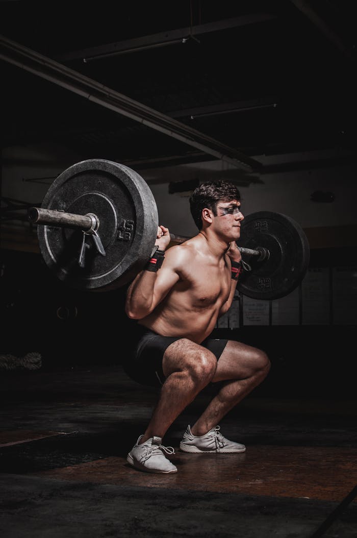 services-04 Shirtless man performing a barbell squat, showcasing strength and fitness.